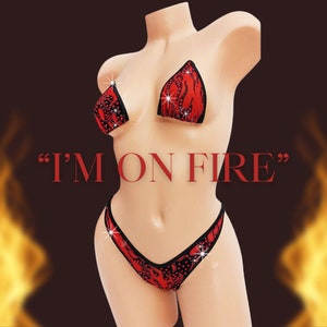 Könnte beinhalten: Roter und schwarzer Bikini mit Flammenmuster und Strasssteinen. Das Bikinioberteil hat transparente Träger. Der Text "I'M ON FIRE" ist in roten Buchstaben auf schwarzem Hintergrund geschrieben.