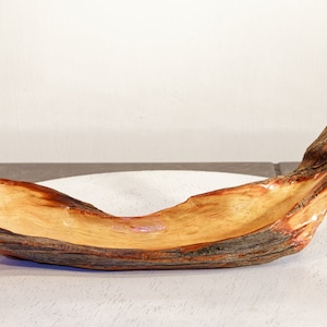 May include: A handcrafted wooden bowl with a natural, organic shape. The bowl is made from a light-colored wood with dark brown bark edges. It sits on a white surface, showcasing its unique, rustic design. This decorative bowl is ideal for home decor.