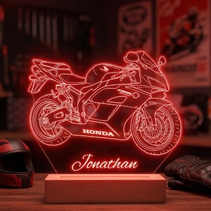 May include: A red LED light display featuring a Honda CBR motorcycle outline and the name Jonathan in script font. The acrylic panel is mounted on a rectangular wooden base, creating a glowing silhouette of the sport bike with visible Honda branding.