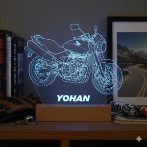 Könnte beinhalten: LED-Nachtlicht mit einer blauen Motorrad-Umrisszeichnung. Der Name "YOHAN" ist auf der Basis zu sehen. Das Licht steht auf einem Holzsockel. Ein dekoratives Element für Motorradfans.