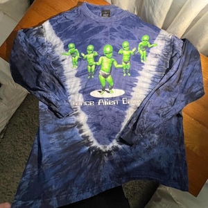 May include: A long-sleeve shirt with a blue and white tie-dye pattern. The front features five green alien figures in diapers, with one centered and larger than the others. Below the figures, the text reads "Dance Alien Dance" in white letters.