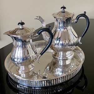 May include: A silver tea set with a teapot, creamer, and sugar bowl on a silver tray with a decorative border.