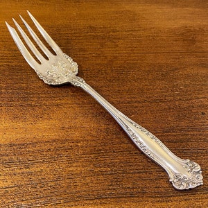 May include: A silver fork with an ornate handle. The fork has four tines and a decorative design on the handle.