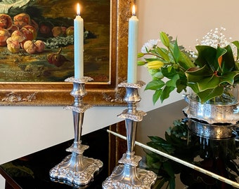 May include: Two silver candle holders with ornate details, each holding a light blue candle. The candles are lit and the holders are on a black surface.