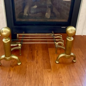May include: A set of brass fireplace tools with a stand. The tools include a poker, tongs, and shovel. The stand has three legs and a round top.