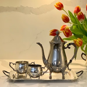 May include: A silver teapot with a silver tray, two silver creamer cups, and a bouquet of orange tulips.