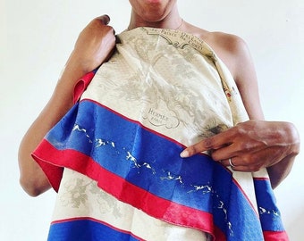 May include: A white silk scarf with a blue and red striped border. The scarf features a vintage illustration of a horse race and the text "Hermes Paris" in a circular frame.