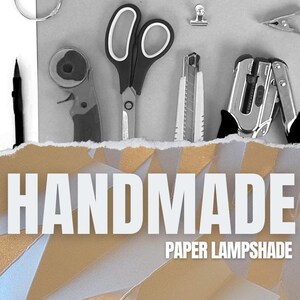 Pu&ograve; includere: Primo piano di strumenti utilizzati per realizzare un paralume di carta. Gli strumenti includono un paio di forbici, un taglierino rotativo, un coltello multiuso, un perforatore e un righello. Gli strumenti sono disposti su una superficie bianca con il testo "HANDMADE PAPER LAMPSHADE" sotto.