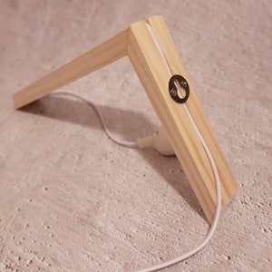 Pu&ograve; includere: Una cornice in legno con un cavo bianco che la attraversa. La cornice ha un occhiello metallico sul lato.