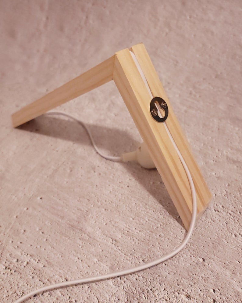 Pu&ograve; includere: Una cornice in legno con un cavo bianco che la attraversa. La cornice ha un occhiello metallico sul lato.