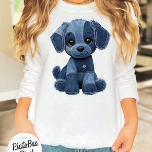 May include: White long-sleeve shirt featuring a denim patchwork dog illustration. The dog has large eyes and a button detail. The design is from PintoBee Pixel. The shirt is a casual style.