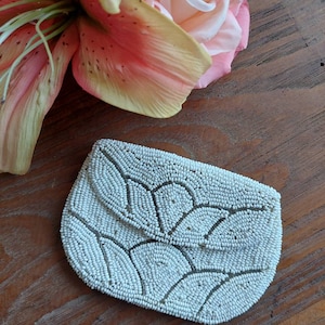 May include: A white beaded coin purse with a floral design. The purse is made of small white beads sewn together in a pattern of overlapping circles.