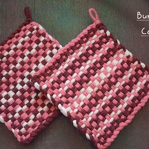 May include: Two square potholders featuring a woven checkerboard pattern in burgundy, carnation pink, and white. Each potholder has a small loop at one corner for hanging. The text Burgundy, Carnation, White is printed on the right side.