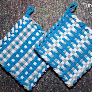 May include: Two square potholders featuring a woven checkerboard pattern in turquoise, silver, and white. Each potholder has a small loop at the top corner for hanging. The text "Turquoise Silver White" is visible in the upper right corner.