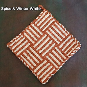 May include: A square, woven pot holder in a geometric pattern of spice brown and winter white. The pot holder has a loop for hanging and the text "Spice & Winter White" is in the upper left corner.