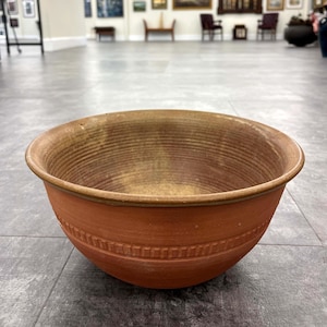 May include: A large, terracotta-colored ceramic bowl with a brown glaze and a decorative rim. The bowl has a wide, shallow shape and is perfect for serving or displaying.