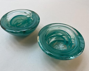 May include: Two teal glass bowls with a swirling pattern. The bowls are made of clear glass with a teal glaze that creates a swirling effect.