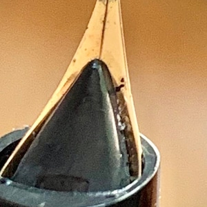 May include: Close-up of a gold-toned fountain pen nib with a black ink cartridge. The nib is pointed and has a fine tip.