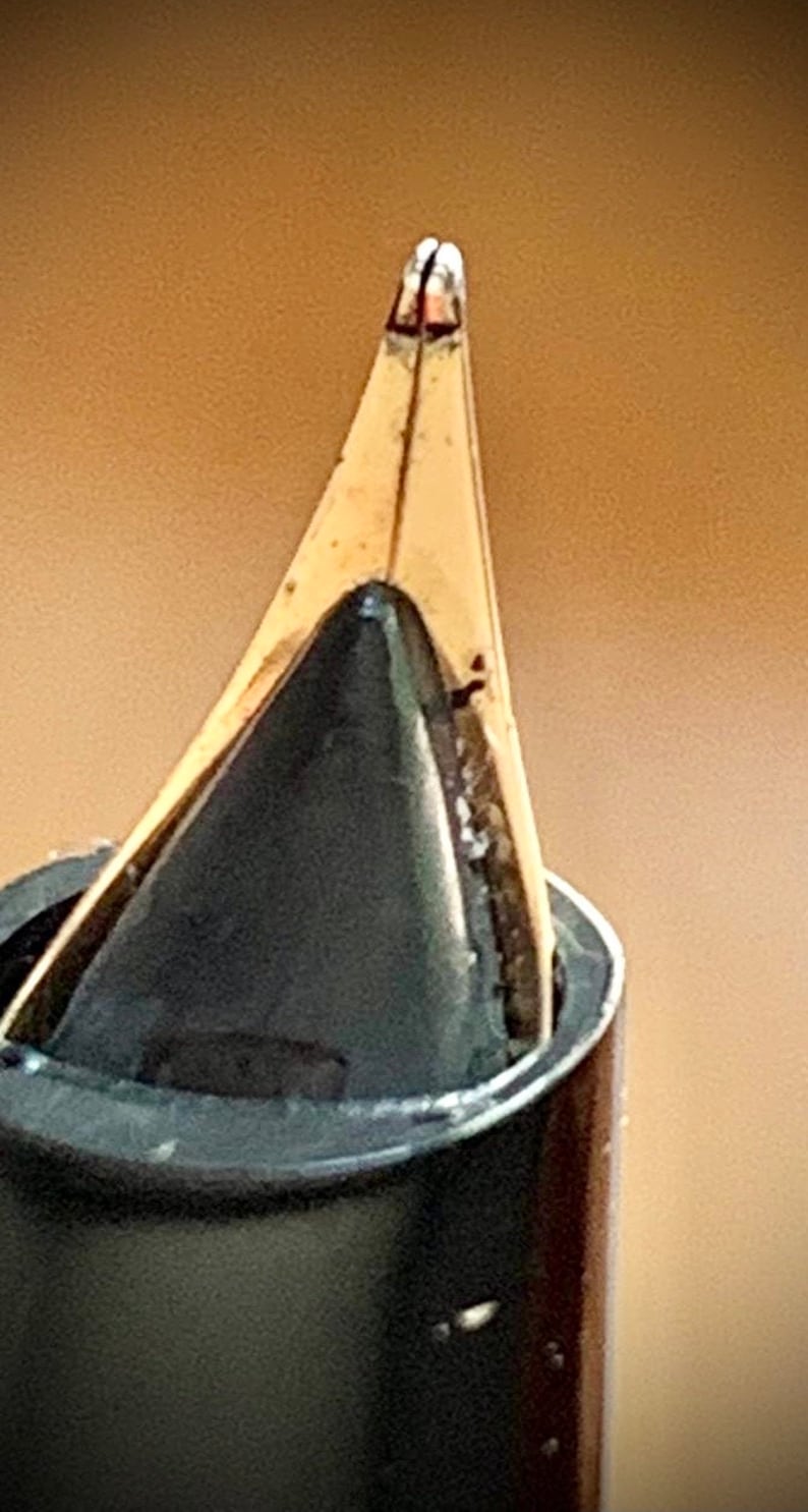 May include: Close-up of a gold-toned fountain pen nib with a black ink cartridge. The nib is pointed and has a fine tip.