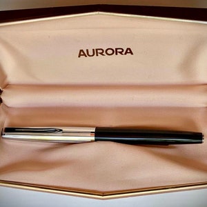 May include: A black and silver Aurora fountain pen in a beige velvet lined box with the word "AURORA" embossed on the lid.