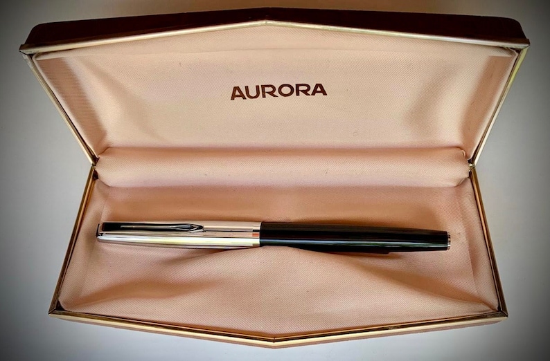 May include: A black and silver Aurora fountain pen in a beige velvet lined box with the word "AURORA" embossed on the lid.