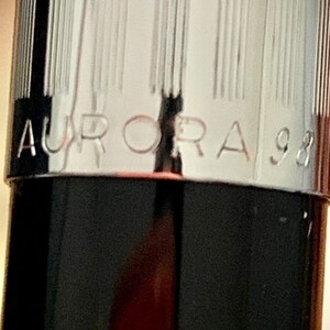 May include: Close-up of a black pen with a silver band that reads "AURORA 98".