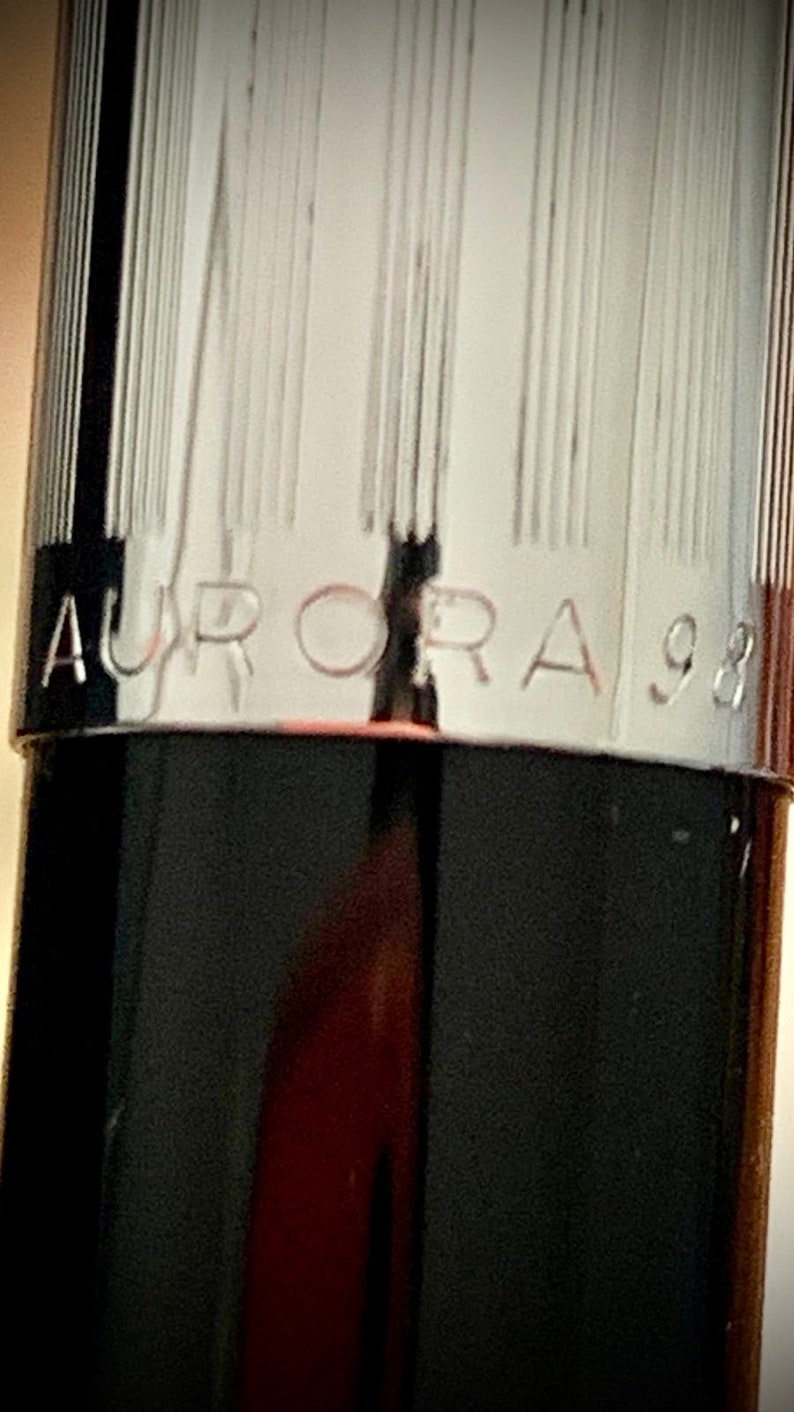 May include: Close-up of a black pen with a silver band that reads "AURORA 98".