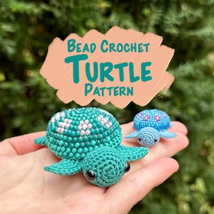 May include: Two crocheted turtle figurines are held in a hand. The larger turtle is teal with white and pink floral details. The smaller turtle is light blue with a blue and pink floral pattern. The image includes the text "Bead Crochet Turtle Pattern."