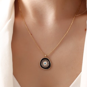 May include: A gold chain necklace with a black and white evil eye pendant. The pendant is round and has a blue eye in the center.