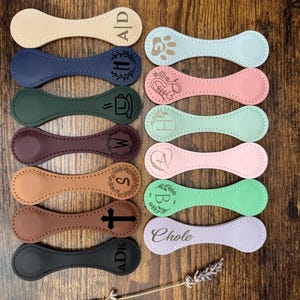 May include: A collection of 12 leather keychains with various designs and text, including initials, a paw print, a coffee cup, a cross, and the word "Chloe".
