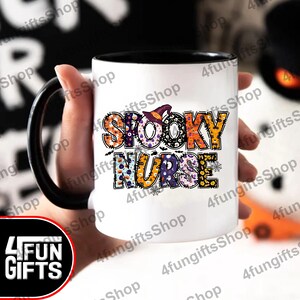 May include: White coffee mug with a black handle and black rim. The mug features a colourful design that says "Spooky Nurse" with a witch's hat on the "O" in "Spooky".
