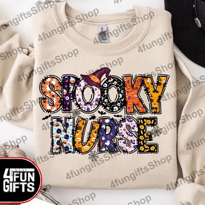 May include: A beige sweatshirt featuring a patchwork design of the words "Spooky Nurse" in black lettering. The letters are decorated with Halloween-themed patterns, including ghosts, pumpkins, bats, and spiders.