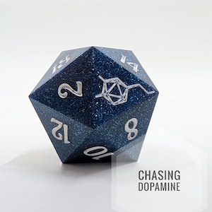 Puede incluir: Un dado D20 azul brillante con números blancos y un diseño de molécula de dopamina. El texto "CHASING DOPAMINE" se muestra en un hexágono blanco. Ideal para juegos de rol.