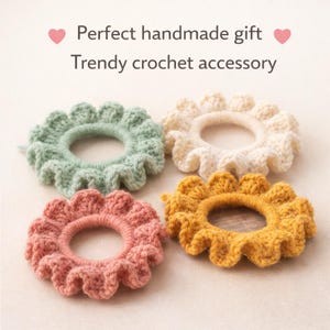 Peut inclure: Quatre chouchous faits à la main en crochet, aux couleurs pastel : vert menthe, crème, rose corail et jaune moutarde. Chaque chouchou présente un motif à volants en forme de fleur. Le texte indique : "Cadeau fait main parfait" et "Accessoire crochet tendance."