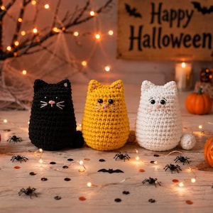 May include: Three crocheted cat figurines in black, yellow, and white. Each cat has small pointed ears, dark round eyes, and embroidered whiskers. The figures are arranged in a row, featuring a rounded body shape and a small tail on the side.