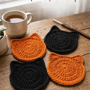 May include: Four round crochet cat coasters in alternating black and orange colors, each featuring two small pointed ears at the top. The text Crochet Cat Coaster is visible at the top of the image, accompanied by a mug and a crochet hook.