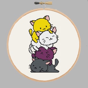 May include: A cross-stitch embroidery project in a circular wooden hoop featuring a vertical stack of four cartoon cats. The cats are colored yellow, white, purple, and dark gray from top to bottom, all with pink inner ears and simple black facial features.
