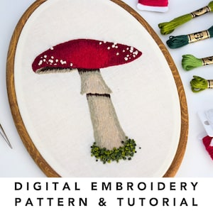 May include: Digital embroidery pattern and tutorial for a red and white mushroom with green accents. The pattern is displayed in a wooden embroidery hoop.