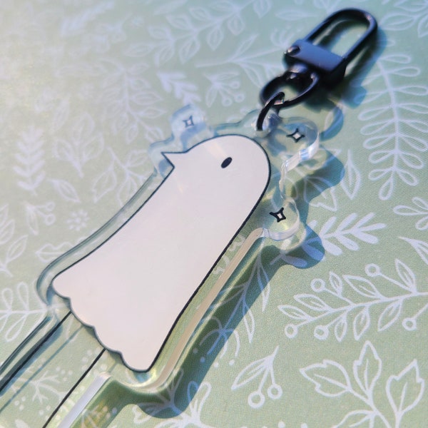 May include: A clear acrylic keychain with a white ghost design. The keychain has a black metal clasp.