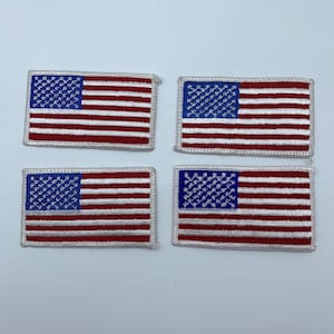 May include: Four embroidered American flag patches with white stitching around the edges. The flags are red, white, and blue.