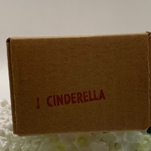 Op de afbeelding: Een bruine kartonnen doos met het woord "CINDERELLA" in rode letters.