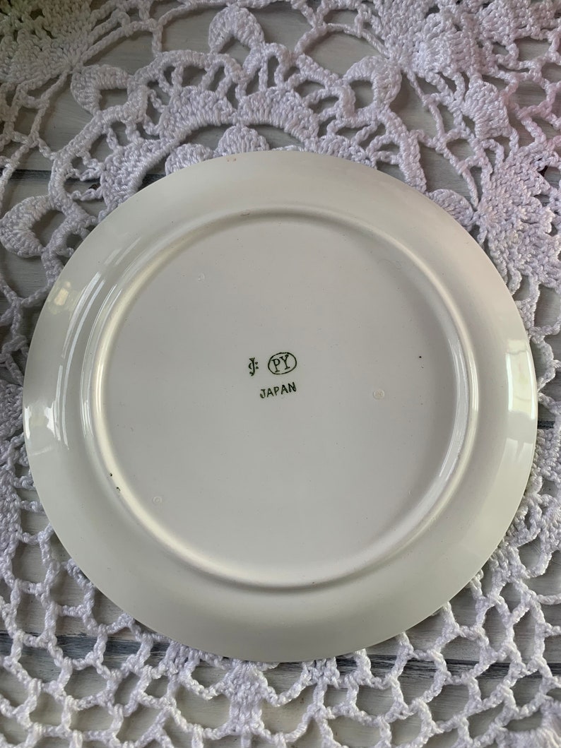 May include: White ceramic plate with a gold rim and a gold inscription that reads "PY JAPAN".
