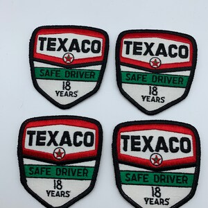 May include: Four vintage Texaco Safe Driver patches. Each patch is a shield shape with a red, white, and green color scheme. The patches feature the Texaco logo, the words "Safe Driver", and the number "18" with the word "Years" underneath.