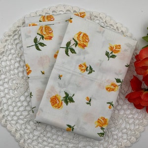 May include: Two white pillowcases with a yellow rose pattern. The pillowcases are folded and placed on a white crocheted doily.