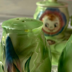 May include: A set of three green ceramic salt and pepper shakers with floral designs. The shakers are decorated with blue, pink, and white flowers.