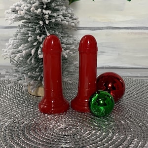 May include: Two red ceramic salt and pepper shakers with a rounded top and a wide base. The shakers are sitting on a silver circular placemat with two red and green Christmas ornaments.