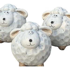 Op de afbeelding: Drie witte keramische schapenfiguren met zwarte ogen en een bruine neus. De schapen staan op een witte achtergrond.