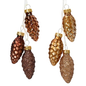 Könnte beinhalten: Sechs gläserne Weihnachtsbaumschmuckstücke in Form von Tannenzapfen. Die Schmuckstücke sind in Braun- und Goldtönen gehalten. Einige der Schmuckstücke haben eine glitzernde Oberfläche.