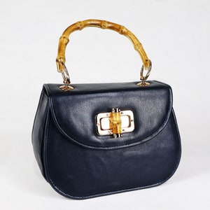 K&ouml;nnte beinhalten: Eine dunkelblaue Ledertasche mit einem Bambusgriff und einem goldenen Verschluss.
