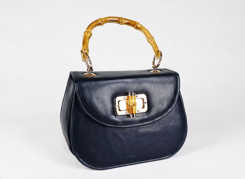 K&ouml;nnte beinhalten: Eine dunkelblaue Ledertasche mit einem Bambusgriff und einem goldenen Verschluss.